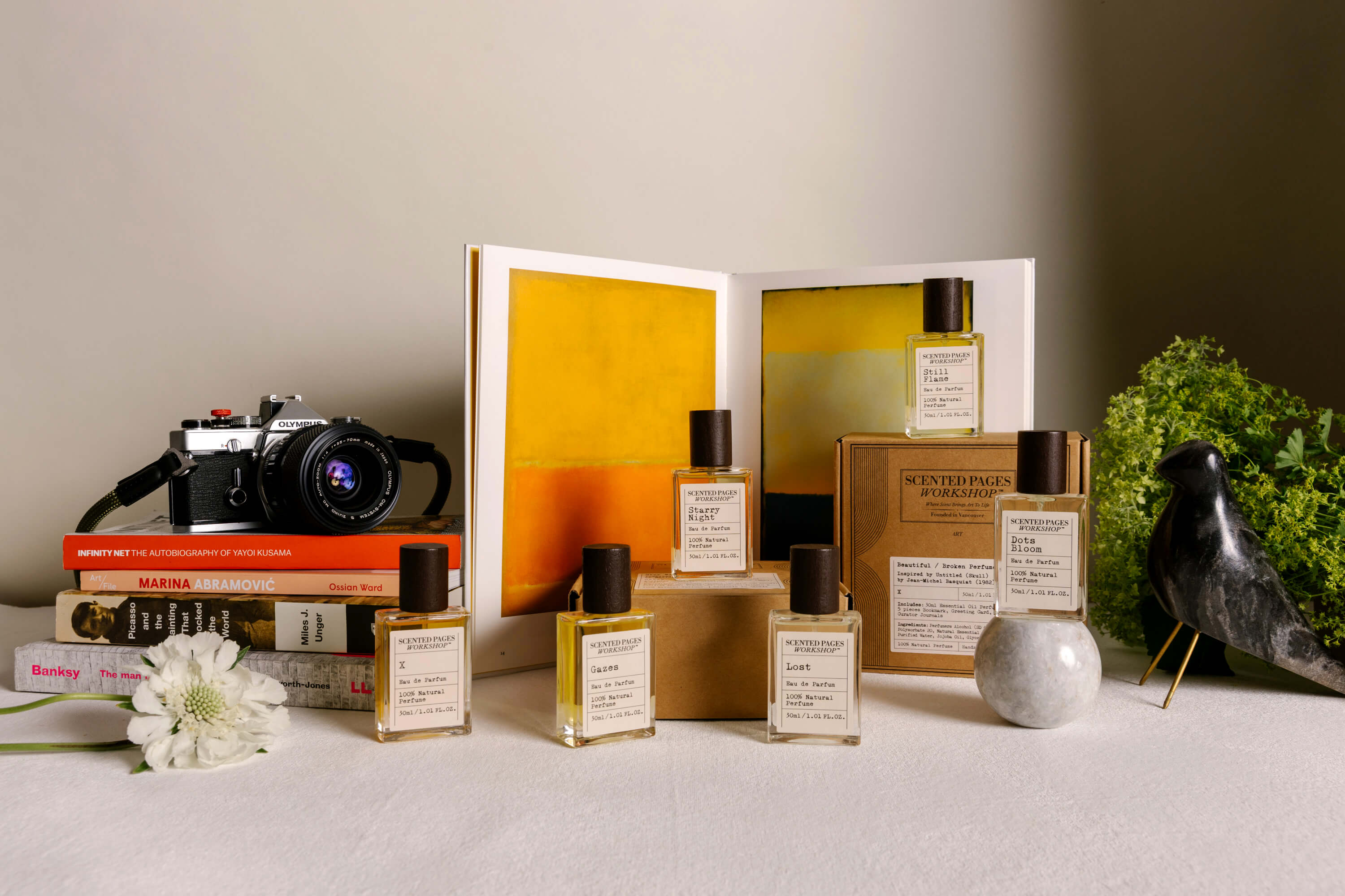 Art-inspired perfume collection by Scented Pages Workshop, with eau de parfum bottles beside books and abstract artwork.